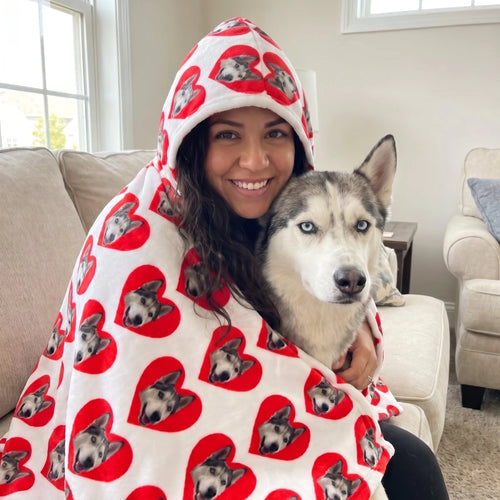 Woman wrapped in a custom pet face hooded blanket cuddling her husky on the sofa