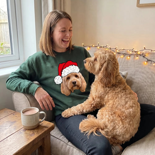 Woman on the sofa in a forest green Santa hat pet face sweatshirt with her cockapoo on her lap