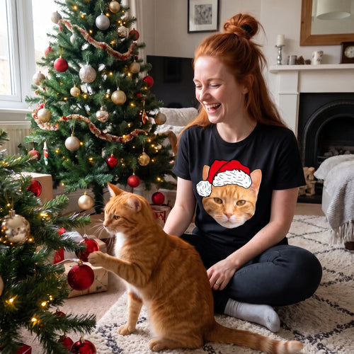 Woman by the Christmas tree in a black Santa hat pet face t-shirt playing with her ginger cat